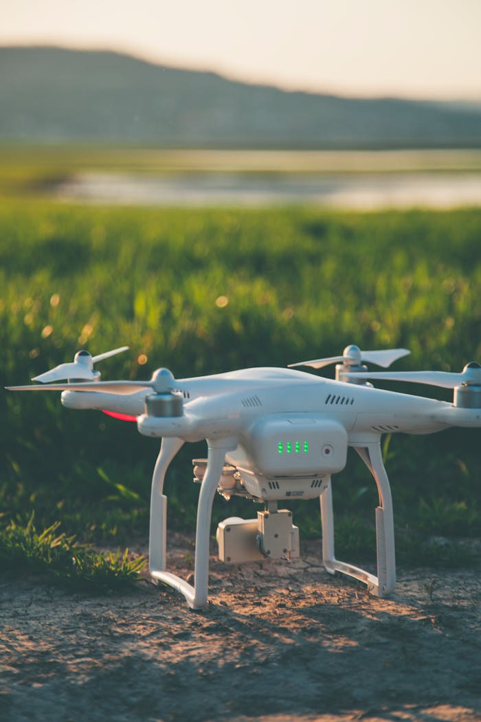 A white drone rests on a grass field during a summer sunset, showcasing technology in nature.
